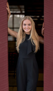 teenage girl standing in between red barn doors looking at the camera and smiling 