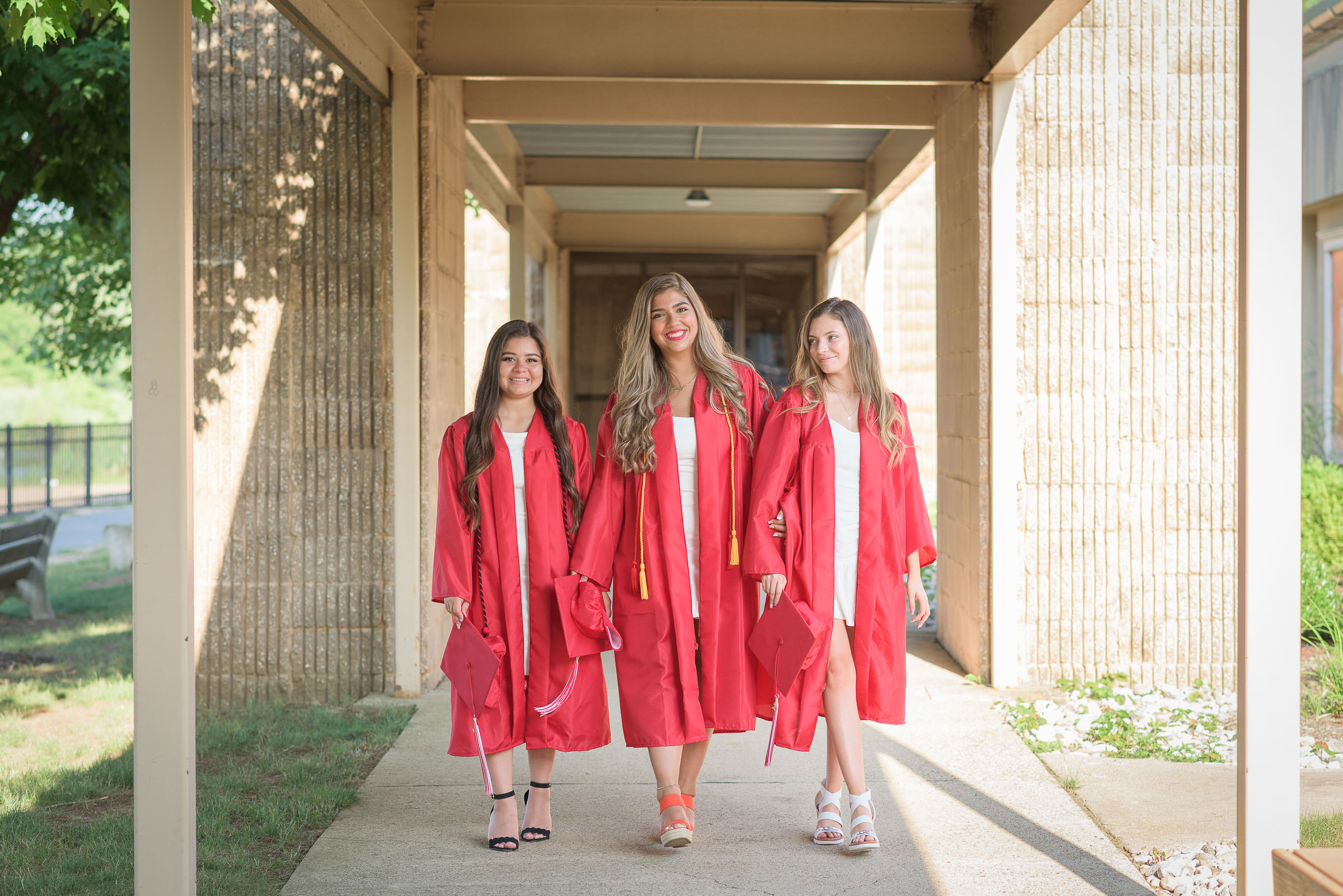 three high school seniors on their red gown celebrating her graduation day and walking towards the camera