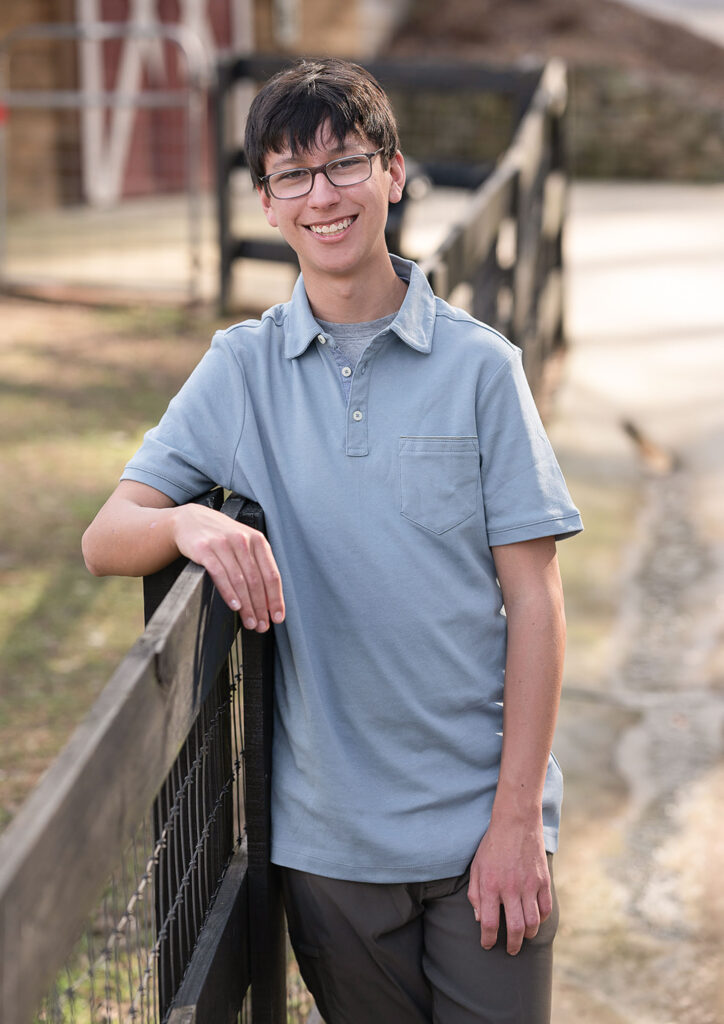 17 year old boy leaning against a fence a posing for his senior photos at a Powder springs Ga farm after receiving his SSAT great score thanks to an Atlanta tutor