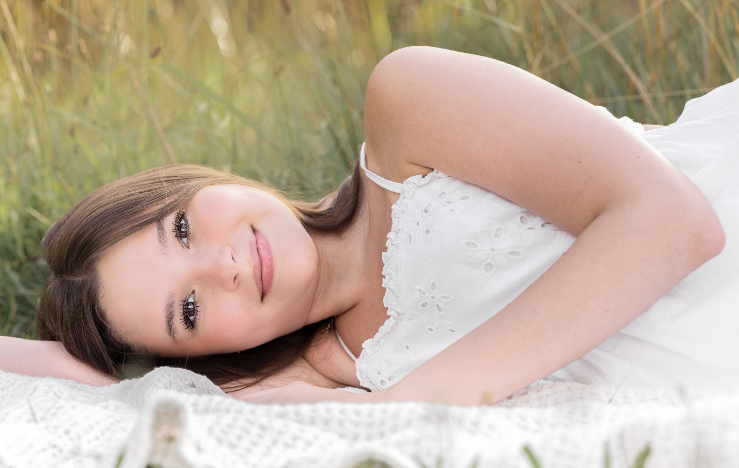 High School junior female laying on the floor on her side smiling at camera and wearing a white dress