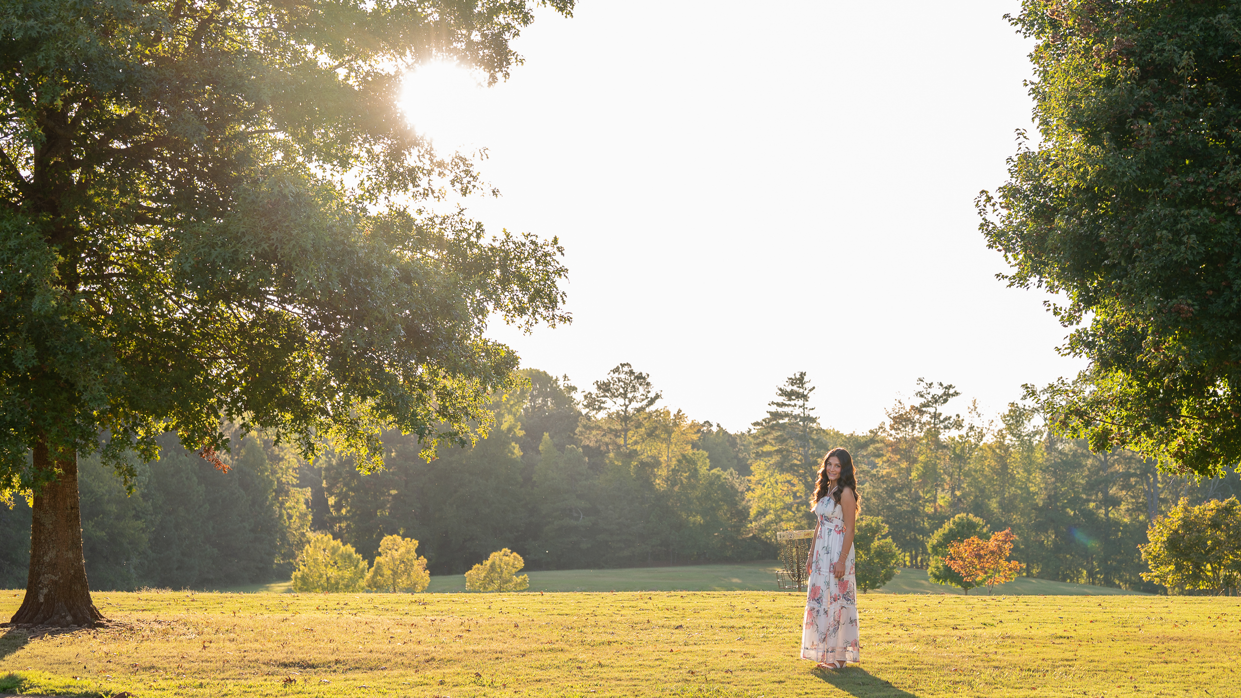 This image shows a girl walking on green field during golden hour, she is wearing a flowy dress with flowers